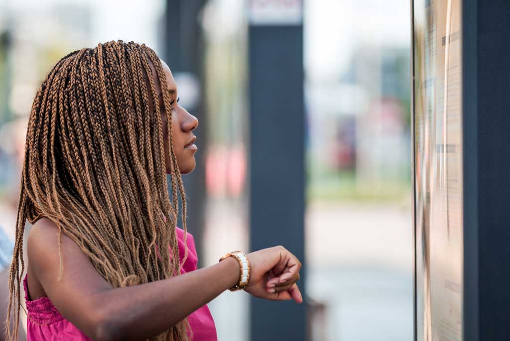 Photo of a woman standing by a bus and looking at a mobile phone